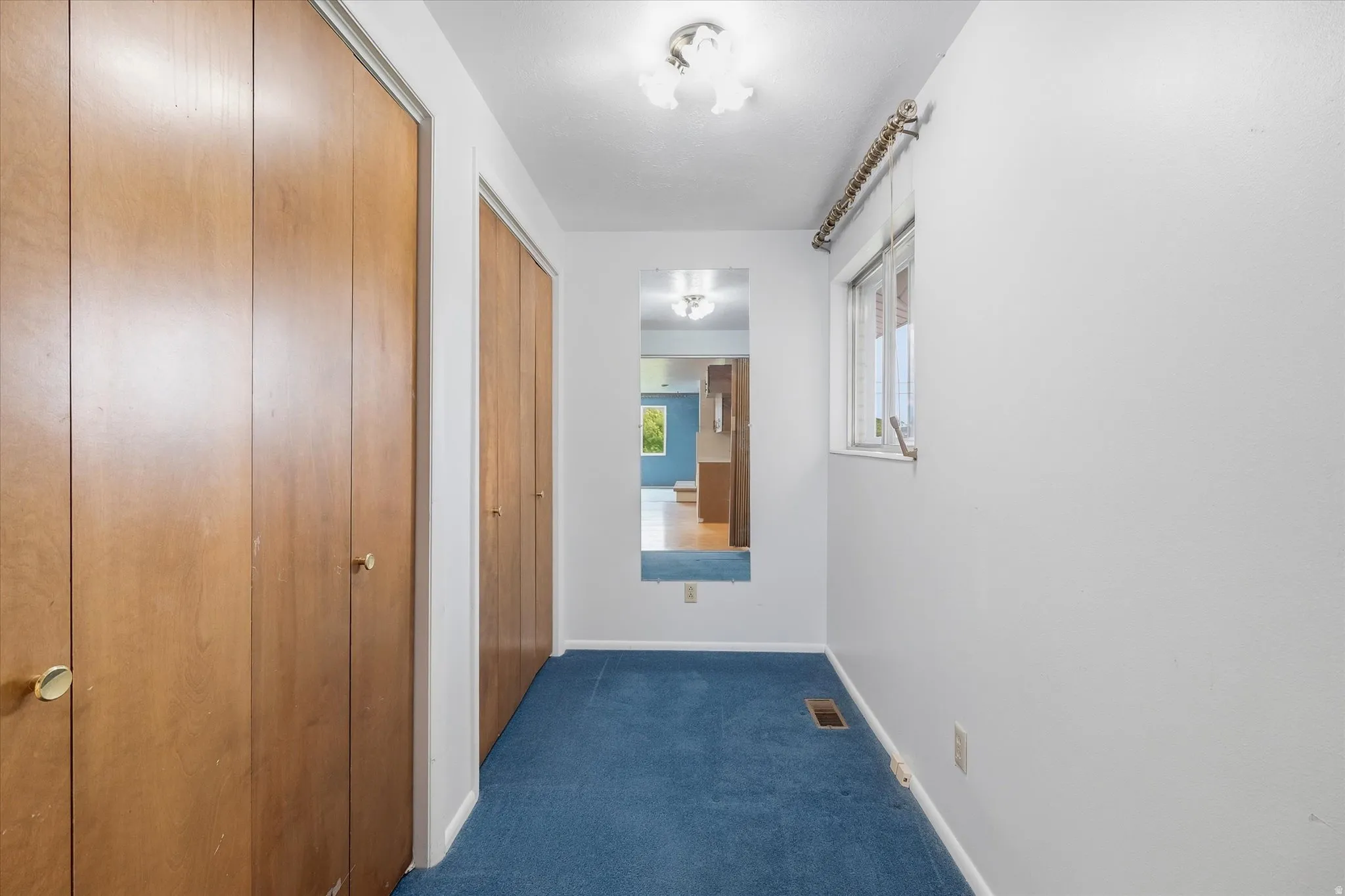 Hallway featuring wood-finish bi-fold doors, blue carpeting, a single window, and a wall-mounted mirror