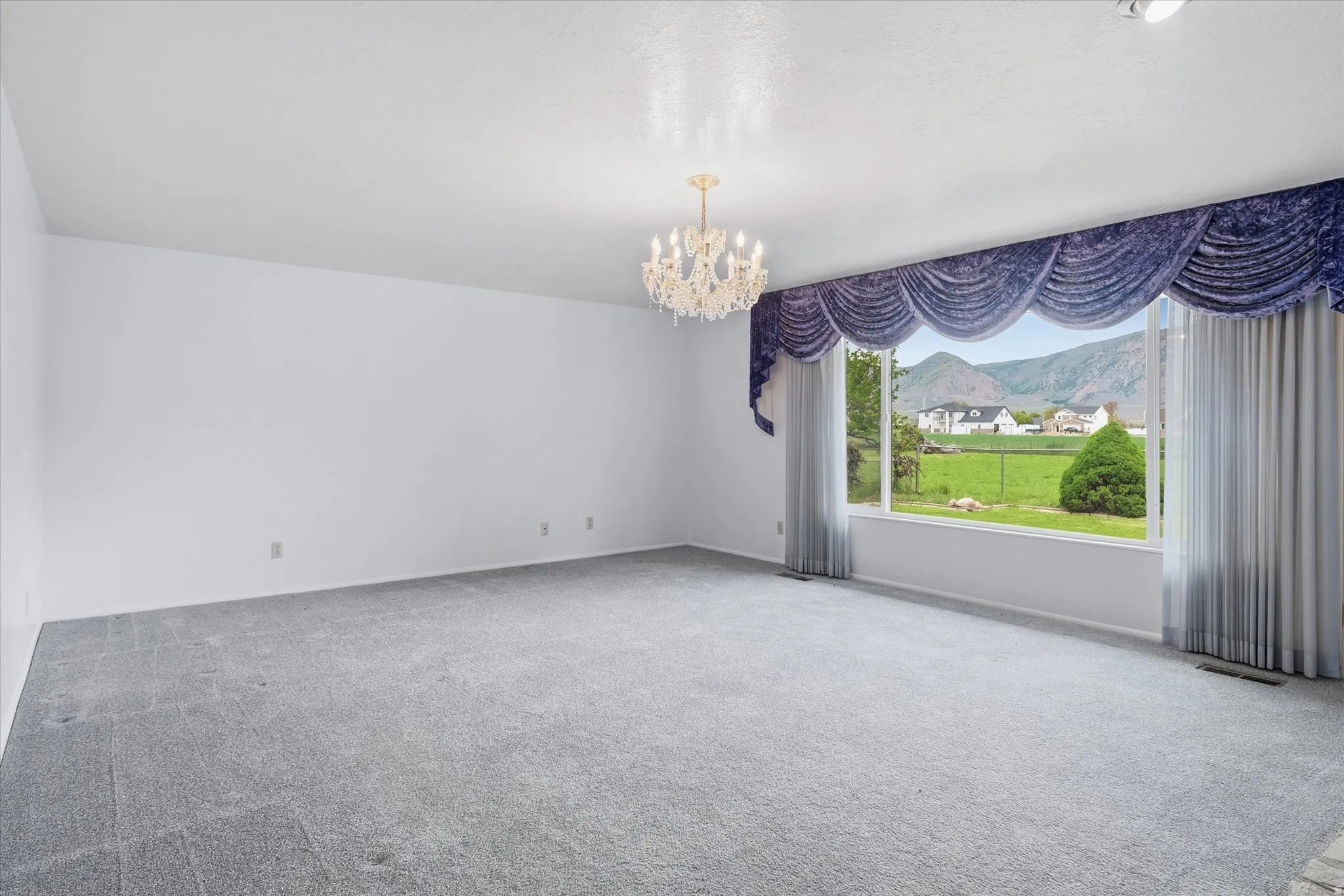 Spacious interior featuring a large picture window, a crystal chandelier, and wall-to-wall carpeting