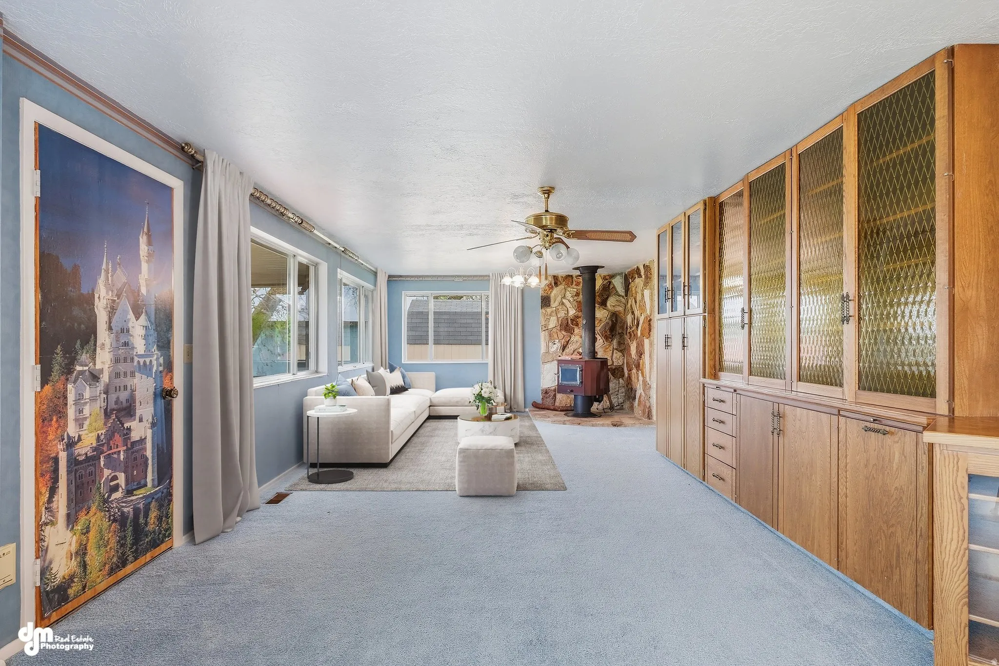 Spacious primary suite featuring extensive wood-finish cabinetry with glass-front display doors, neutral wall-to-wall carpeting, ceiling fan, and abundant natural light from multiple windows