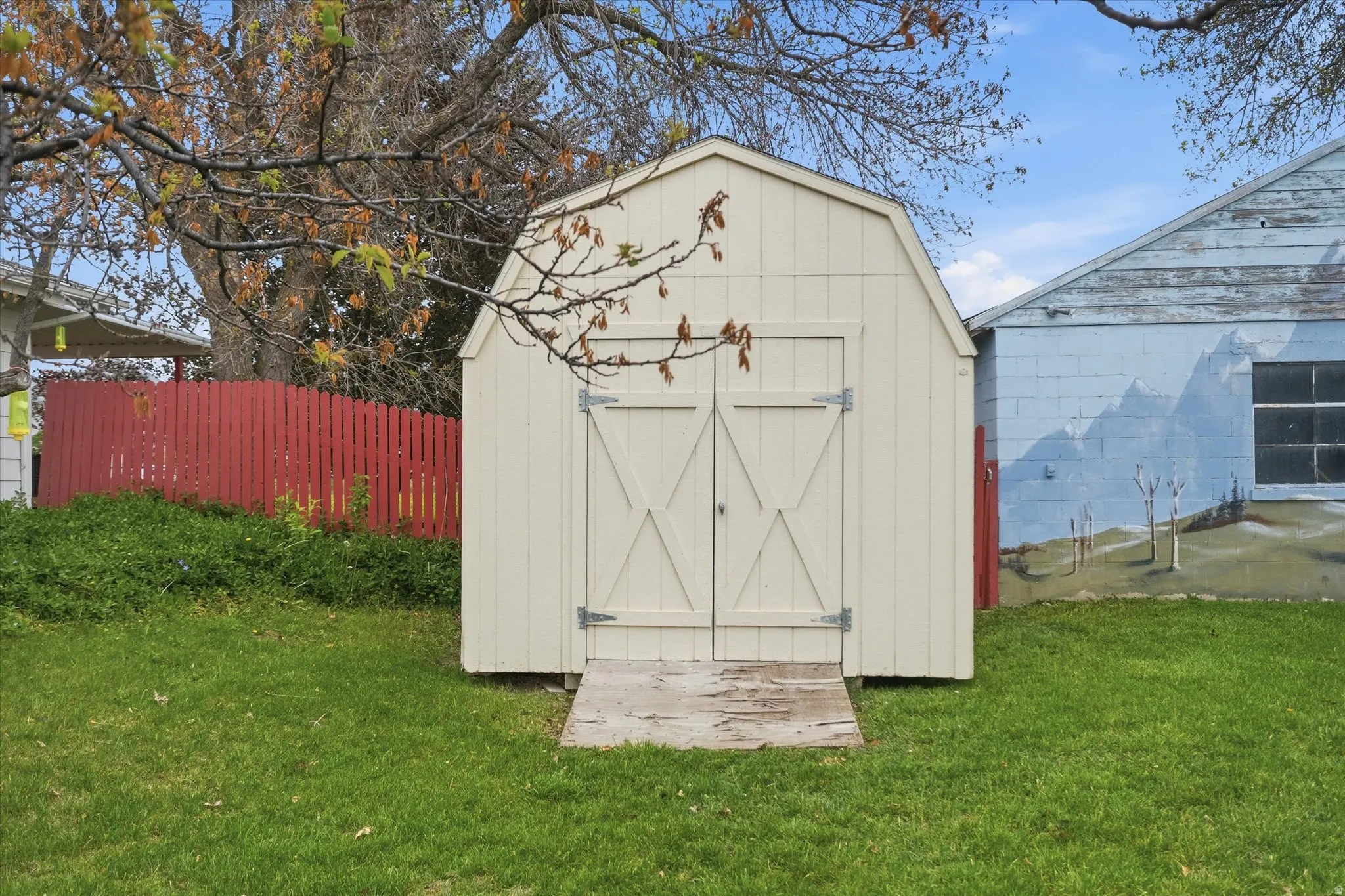 Cream-colored storage shed featuring barn-style double doors and a wooden ramp