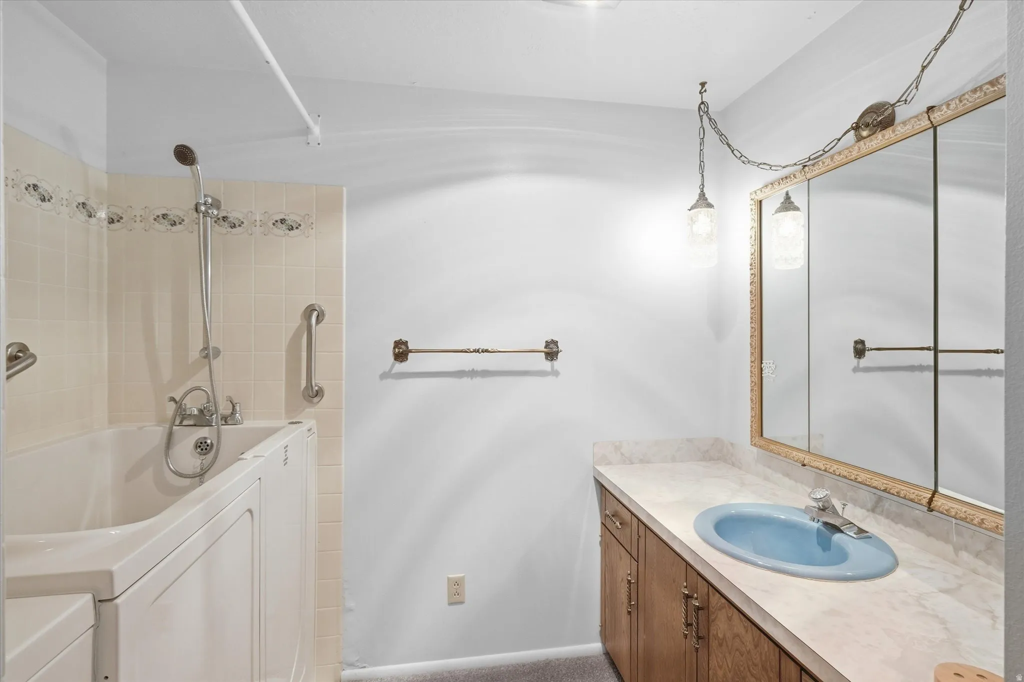 Bathroom featuring a walk-in tub with grab bars, tiled shower surround, wood-finish vanity with a light blue basin, and a mirrored medicine cabinet