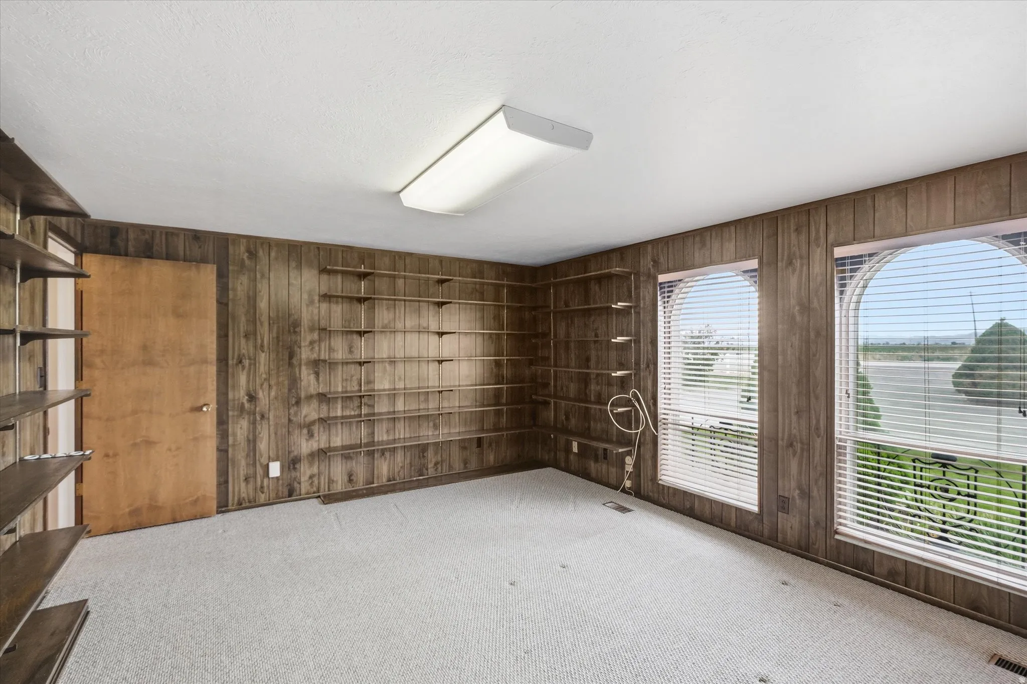 Room featuring wood-paneled walls, built-in shelving, two arched windows with blinds, and light-colored carpeting