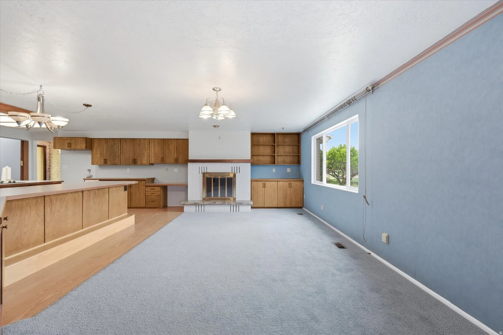 Open-concept living area featuring a fireplace with a decorative mantel, light wood-finish cabinetry, built-in shelving, and a large window