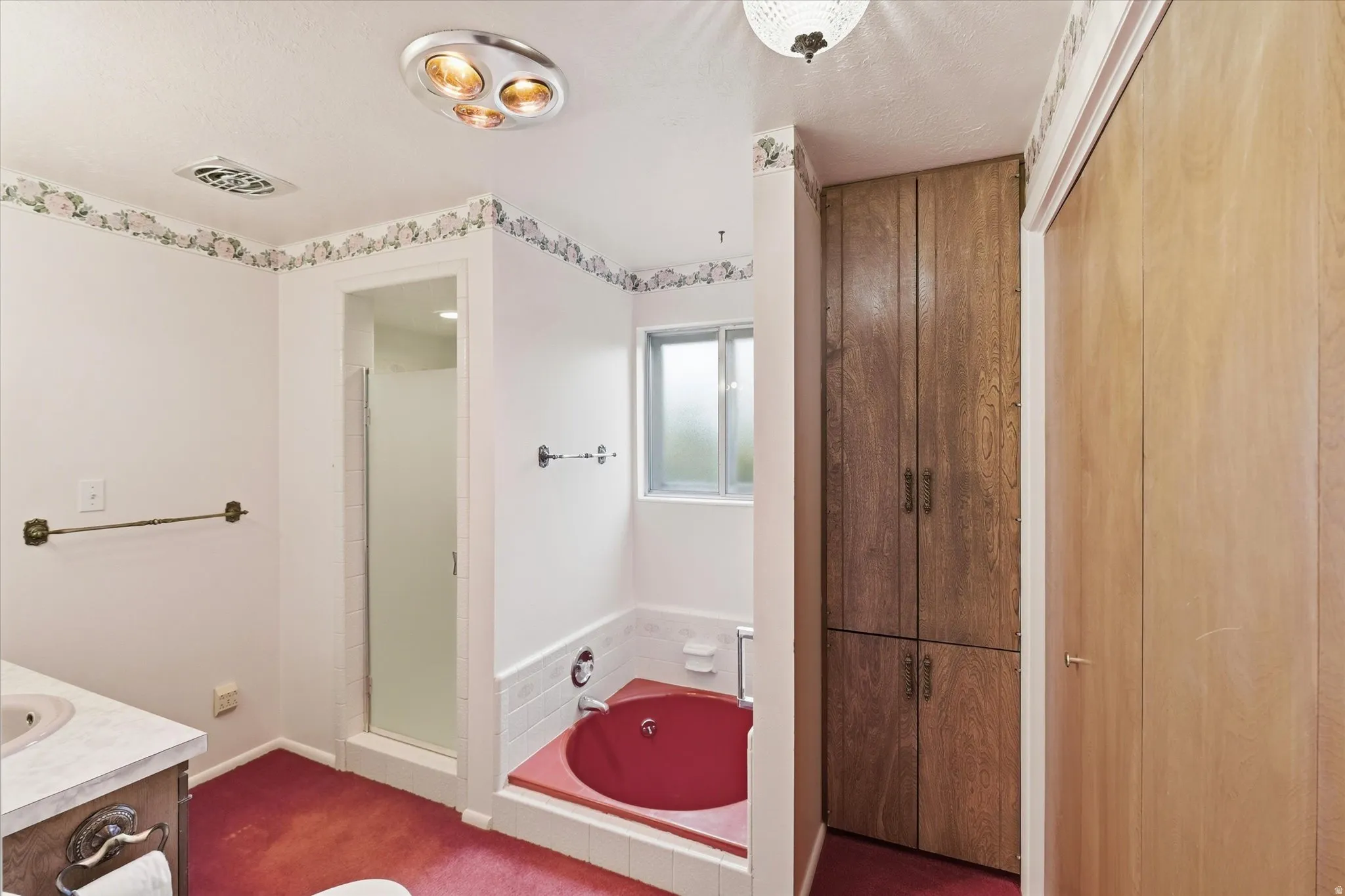 Bathroom featuring a built-in red soaking tub, a stand-up shower with frosted glass enclosure, and a built-in wood-finish storage cabinet