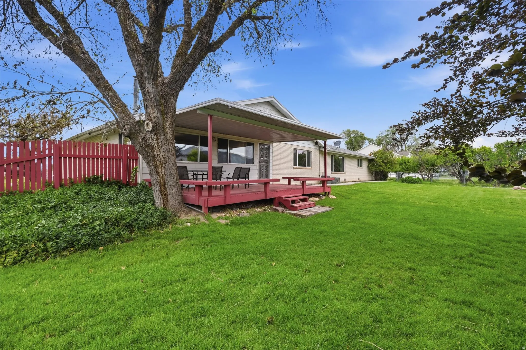 Green lawn with a covered wood deck and red picket fencing