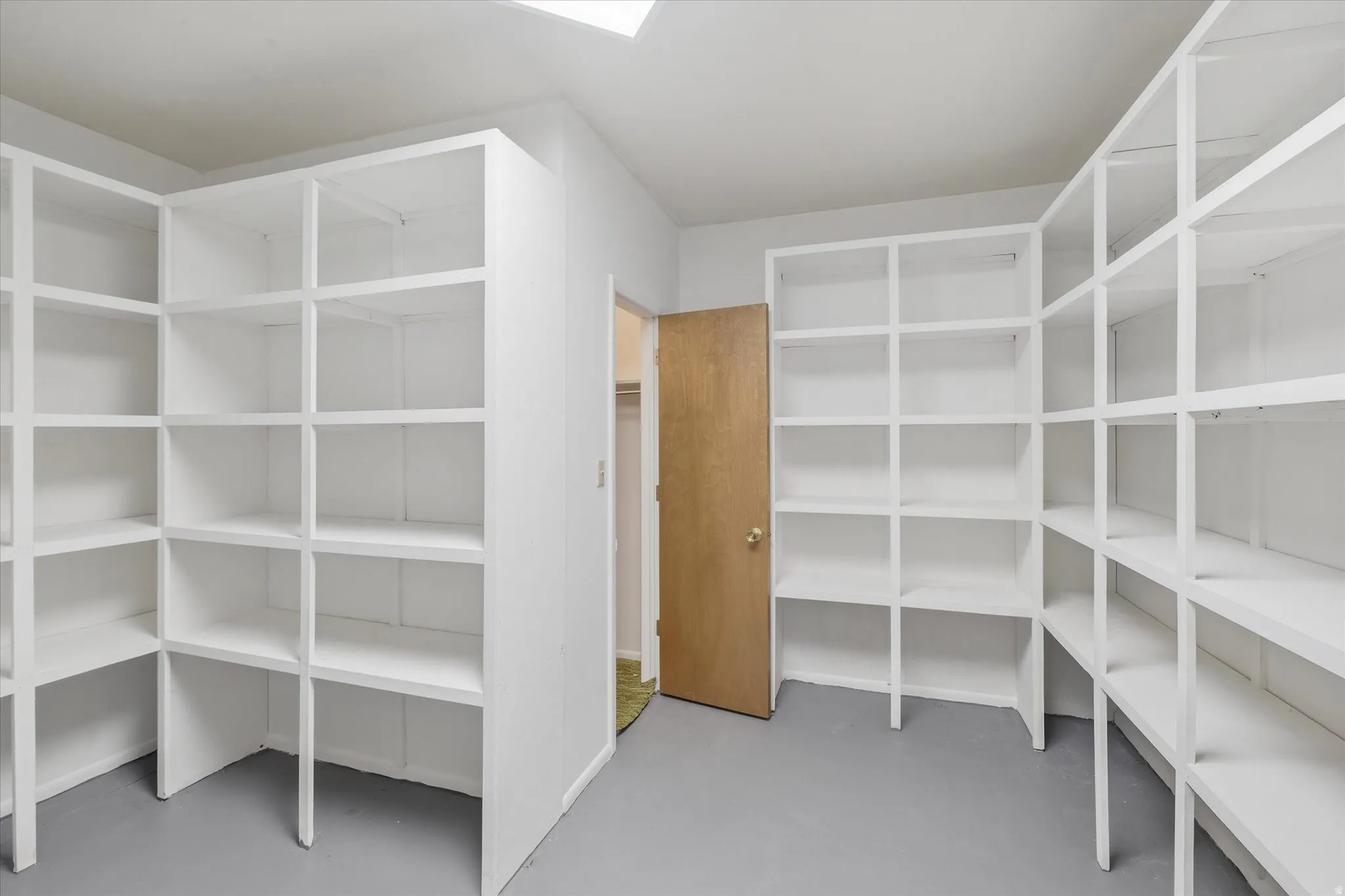 Storage room featuring extensive built-in shelving, a light wood-finish door, and neutral flooring