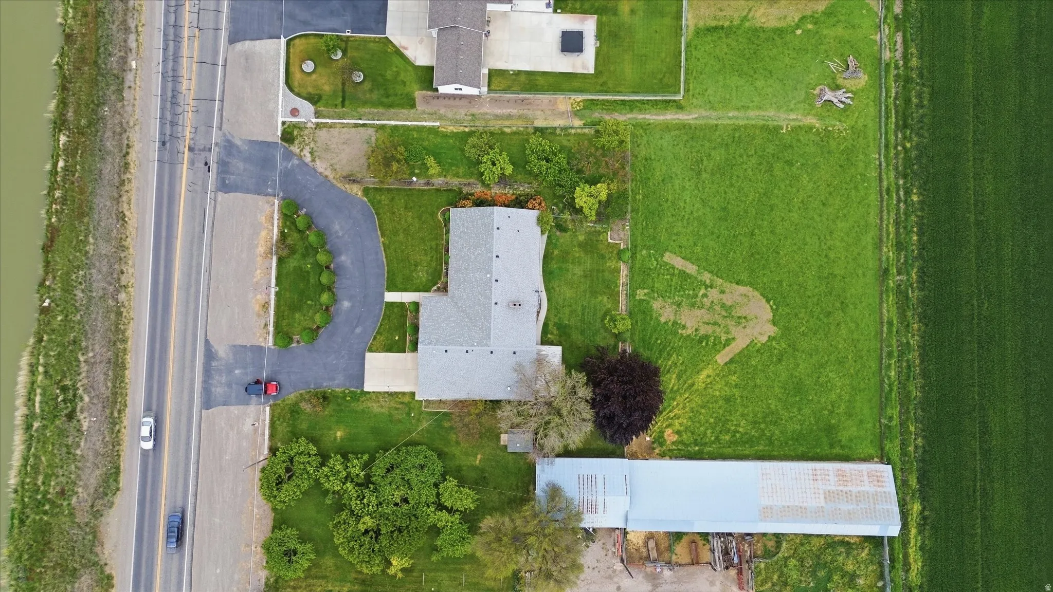 Large lot featuring a main residence with a gray shingle roof, a paved driveway, and a large metal-roofed outbuilding
