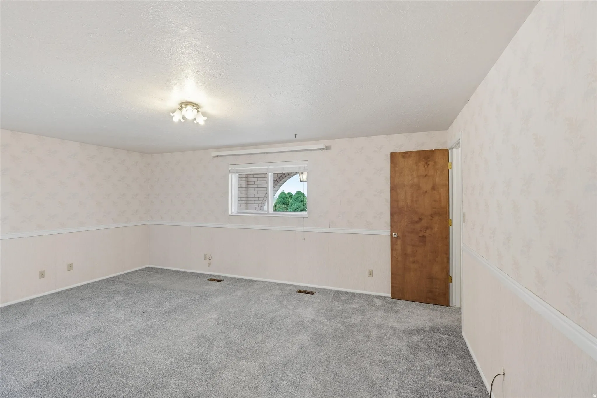 Carpeted room featuring a light-toned ceiling, a window with exterior brick arch detail, and a wood-finish door