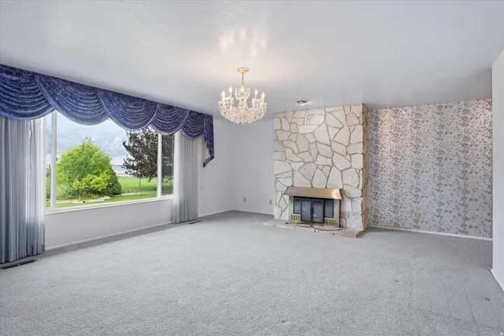 Spacious living area featuring a large picture window, stone-clad fireplace with brass surround, textured accent wall, and a crystal chandelier