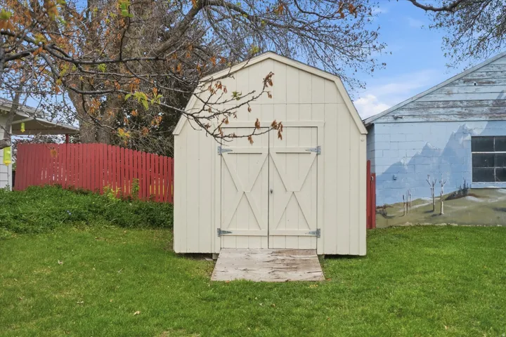 Cream-colored storage shed featuring barn-style double doors and a wooden ramp