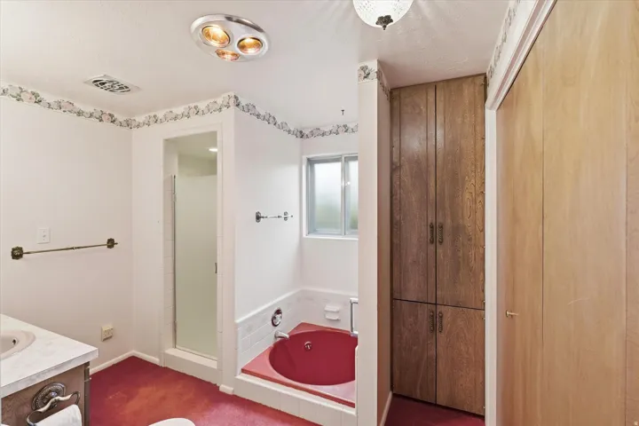 Bathroom featuring a built-in red soaking tub, a stand-up shower with frosted glass enclosure, and a built-in wood-finish storage cabinet