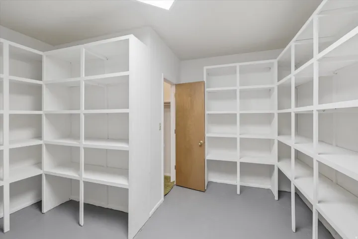 Storage room featuring extensive built-in shelving, a light wood-finish door, and neutral flooring