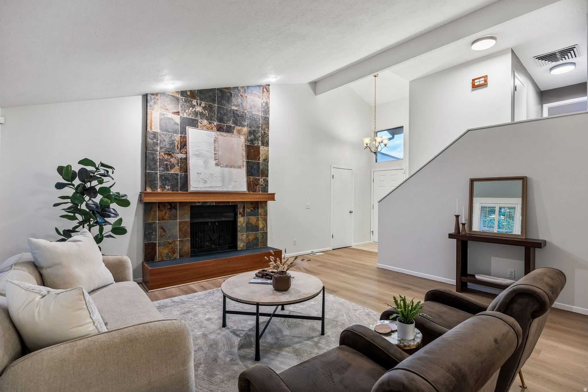 Living area featuring a floor-to-ceiling slate tile fireplace surround with a wood mantel, vaulted ceilings, wood-finish flooring, and a stairway with a partial wall