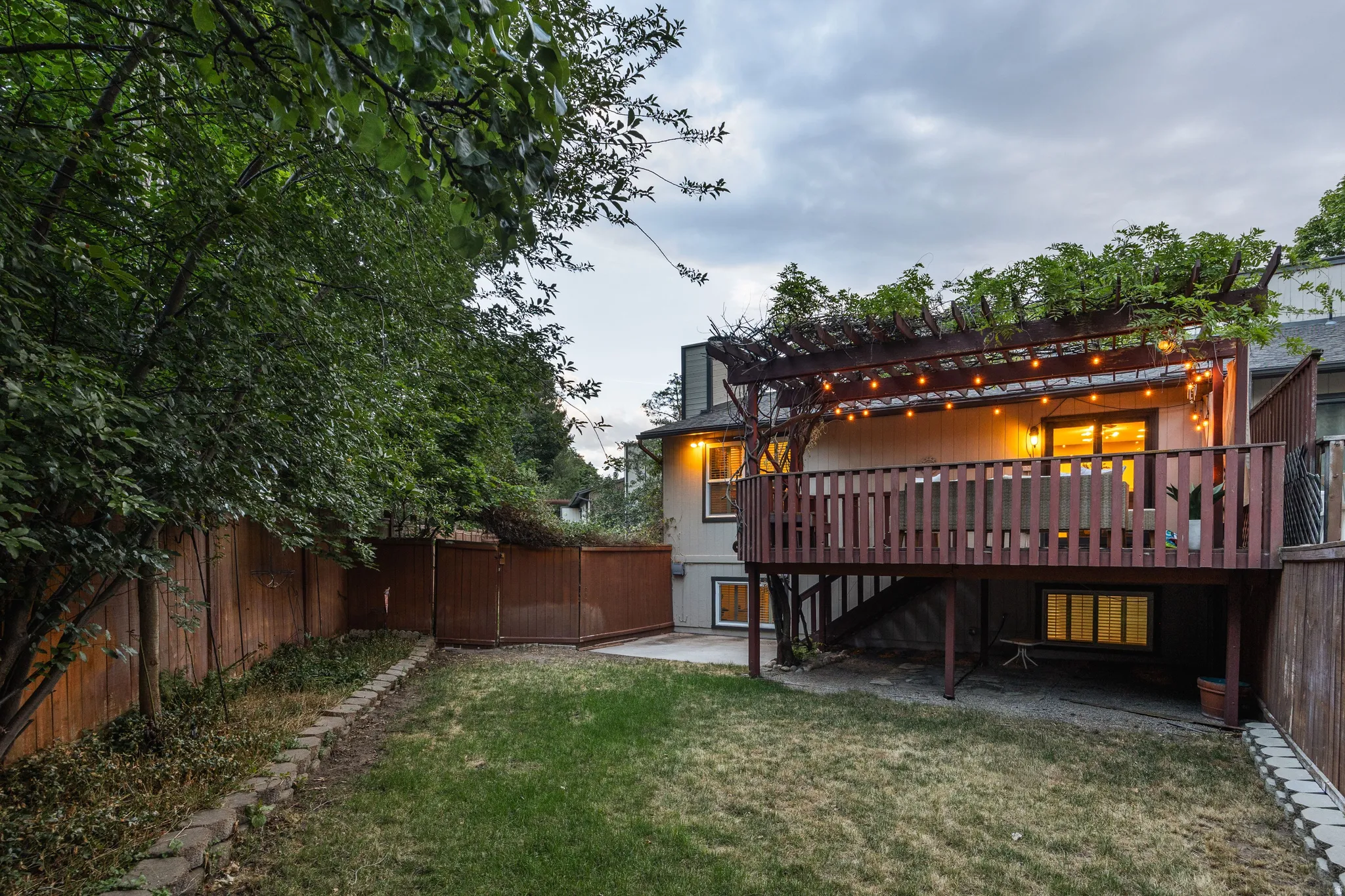 Expansive backyard featuring a tiered wooden deck with a slatted railing and a pergola, mature perimeter trees, and a wooden privacy fence