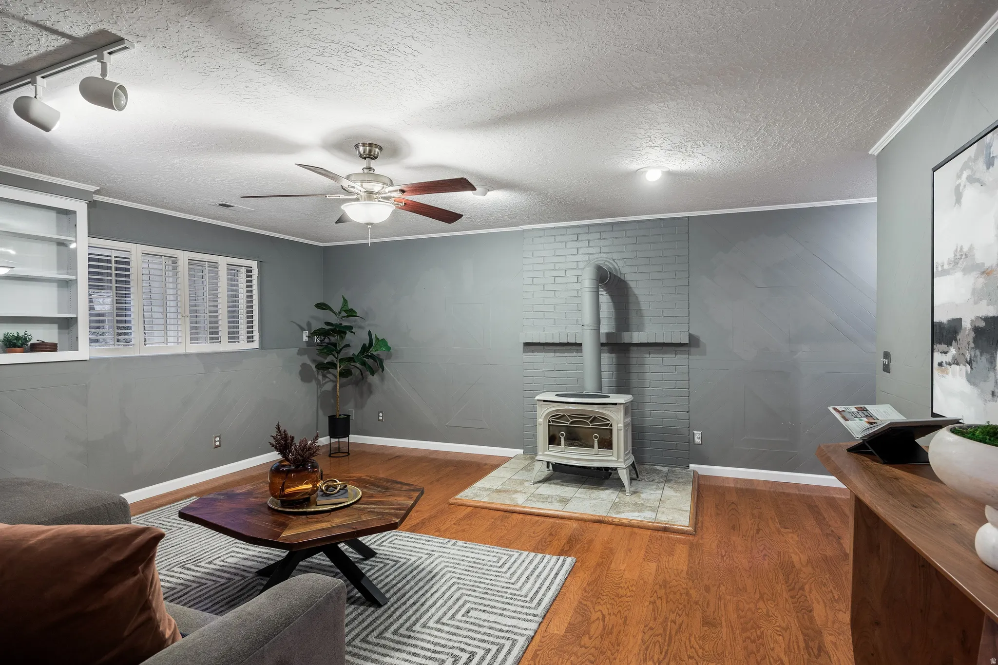 Living area featuring wood-finish flooring, a painted brick accent wall, and an antique-style wood-burning stove with a tile hearth