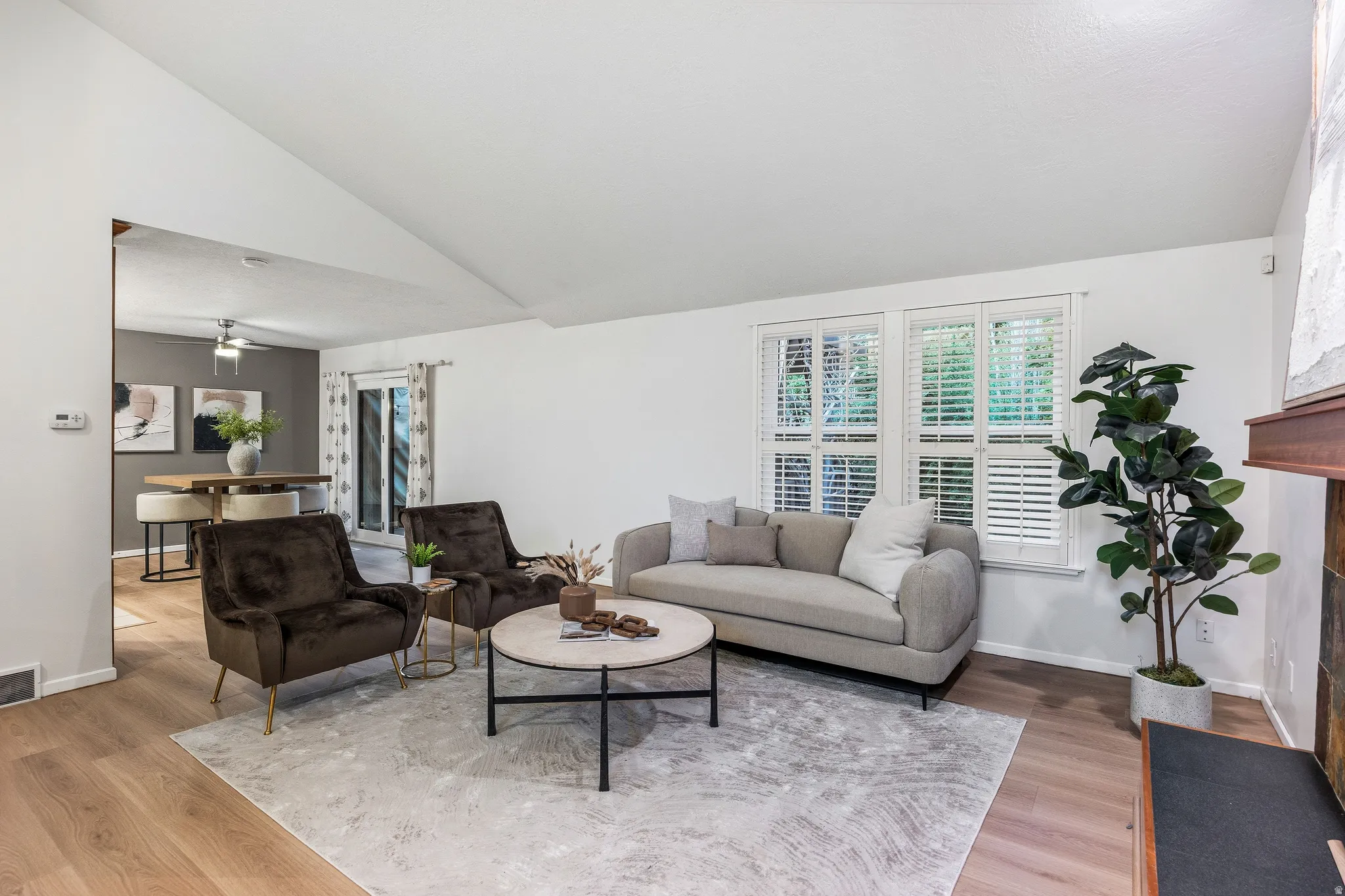 Living space featuring wood-finish flooring, vaulted ceiling, and multiple windows with plantation shutters