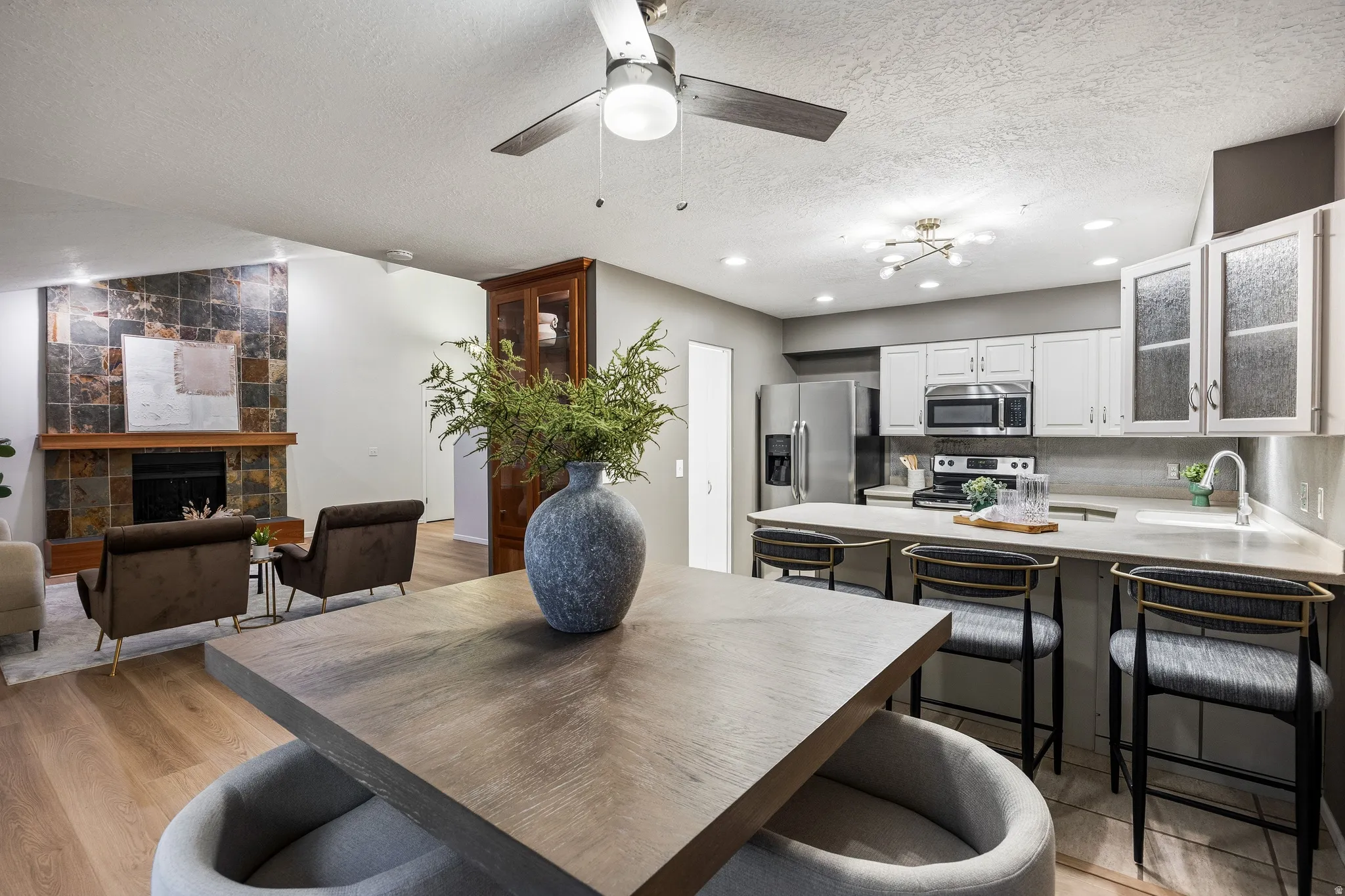 Open-concept living space featuring wood-finish flooring, a contemporary kitchen with stainless steel appliances, and a living area with a stone-accented fireplace