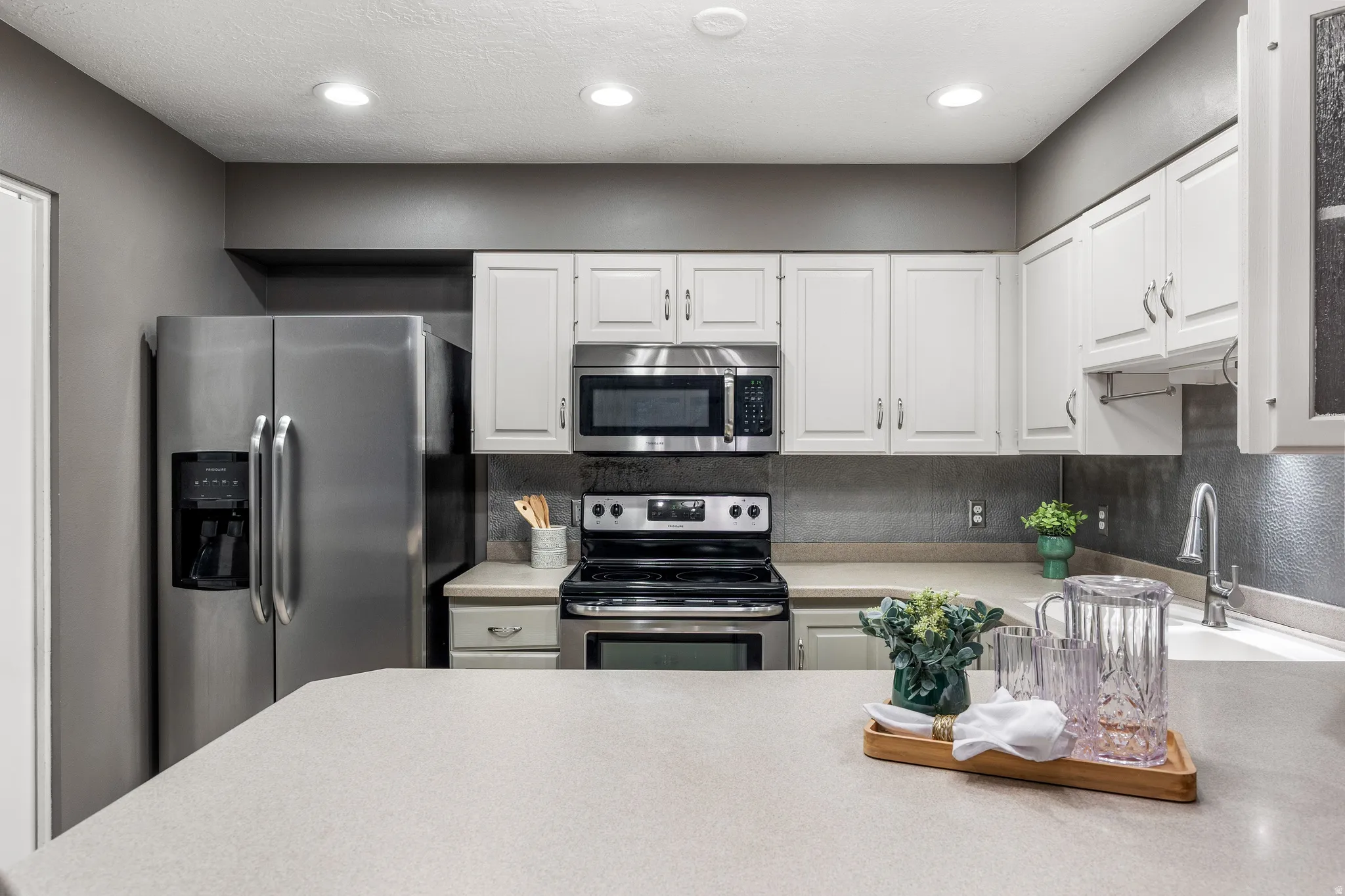 Kitchen featuring stainless steel appliances, white cabinetry, light countertops, a textured backsplash, and recessed lighting