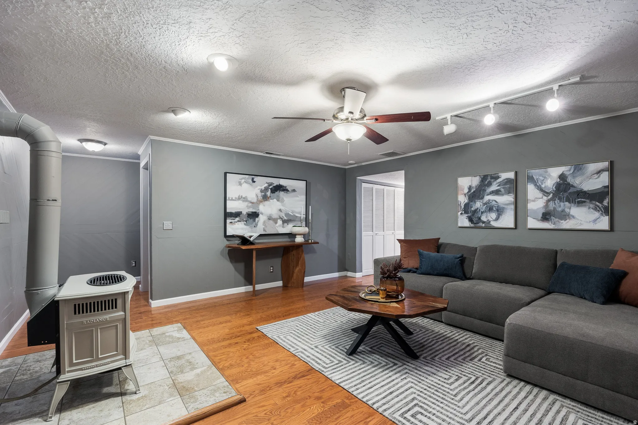 Living area featuring wood-finish flooring, a freestanding stove on a tiled hearth, a ceiling fan, and track lighting