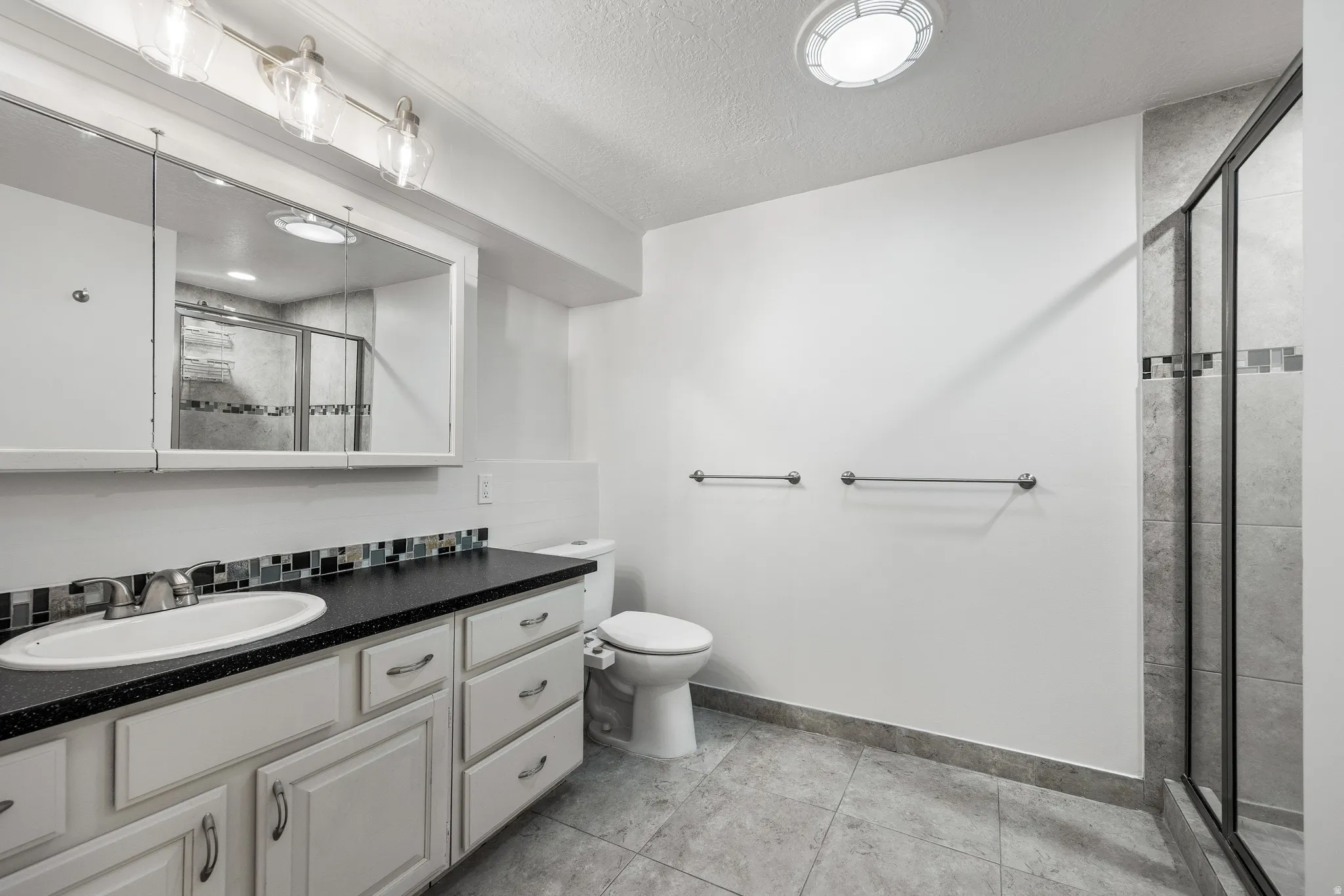 Bathroom featuring a white vanity with multiple drawers, a dark countertop, and an oval sink