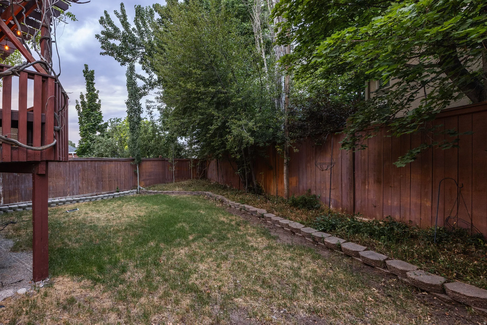 Expansive backyard featuring a manicured lawn, established trees, and a privacy fence