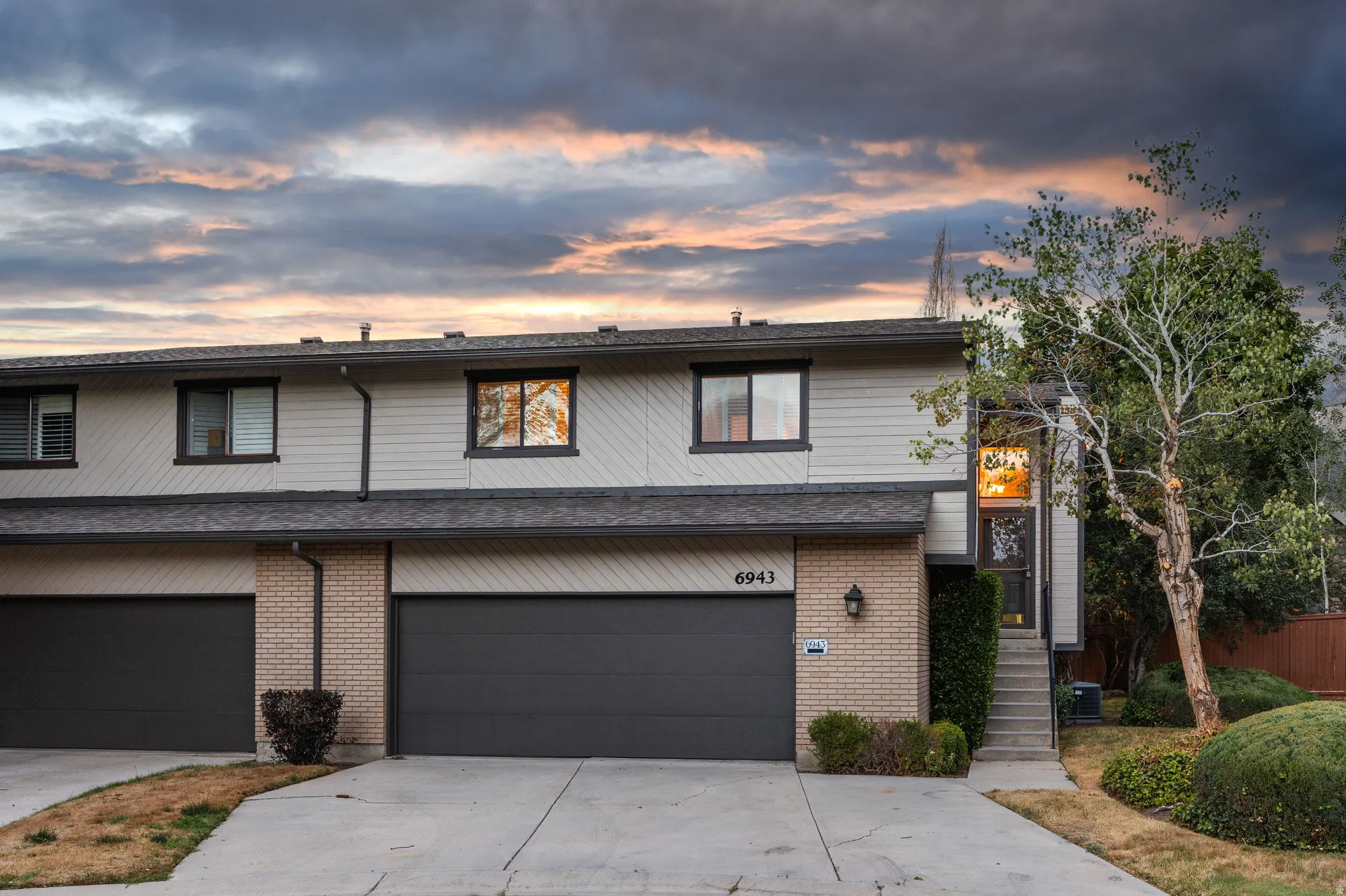 Two-story townhouse exterior featuring a two-car garage, light-colored siding, and brick accents