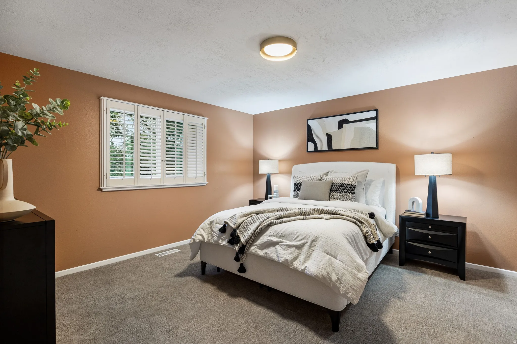 Bedroom featuring a window with white louvered shutters, warm-toned walls, and grey carpet flooring