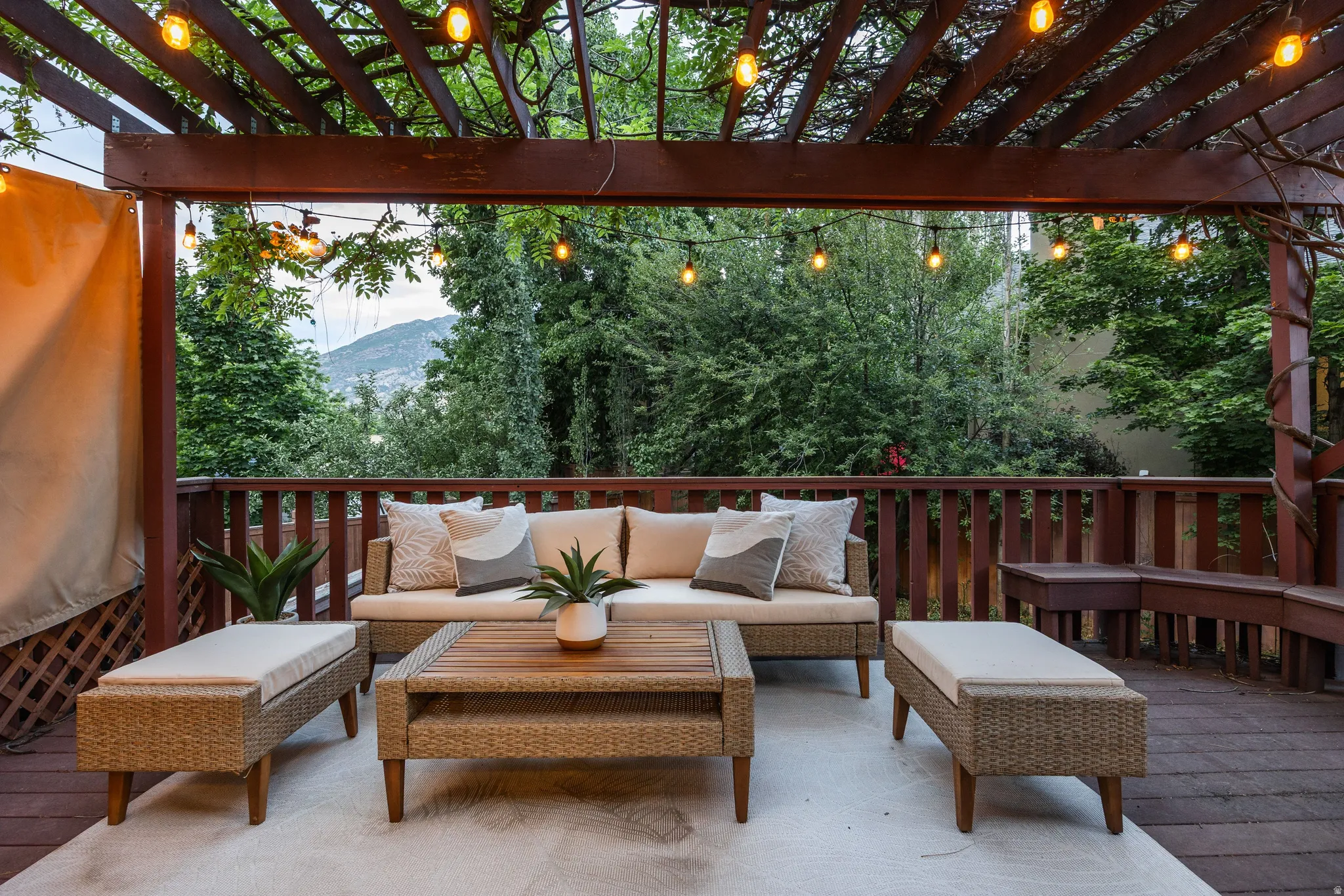 Spacious outdoor deck featuring a wooden pergola, string lights, a wood-finish railing, and built-in bench seating