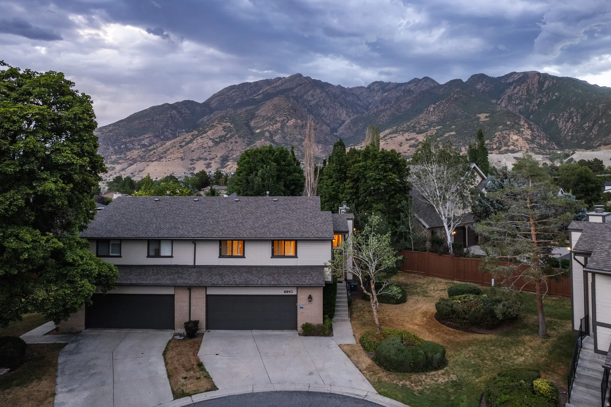 Townhome exterior featuring a pitched shingle roof, attached garage, and mature landscaping