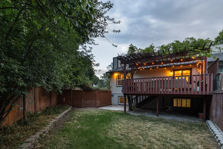 Expansive backyard featuring a manicured lawn, wood fencing, and a stone retaining wall