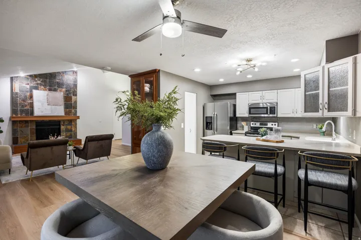 Open-concept living space featuring wood-finish flooring, a contemporary kitchen with stainless steel appliances, and a living area with a stone-accented fireplace
