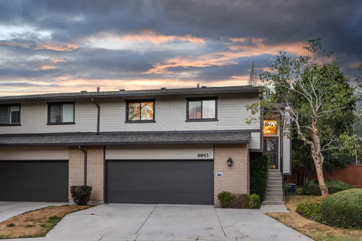 Two-story townhouse exterior featuring a two-car garage, light-colored siding, and brick accents