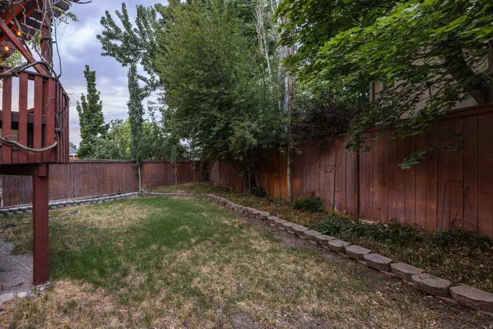 Expansive backyard featuring a manicured lawn, established trees, and a privacy fence