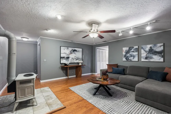 Living area featuring wood-finish flooring, a freestanding stove on a tiled hearth, a ceiling fan, and track lighting