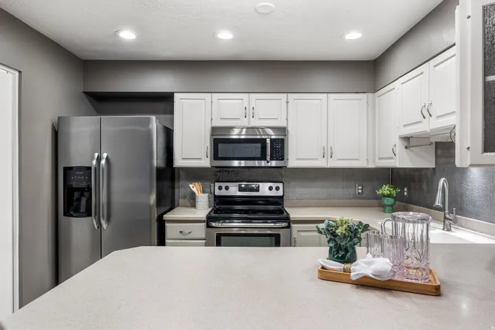 Kitchen featuring stainless steel appliances, white cabinetry, light countertops, a textured backsplash, and recessed lighting