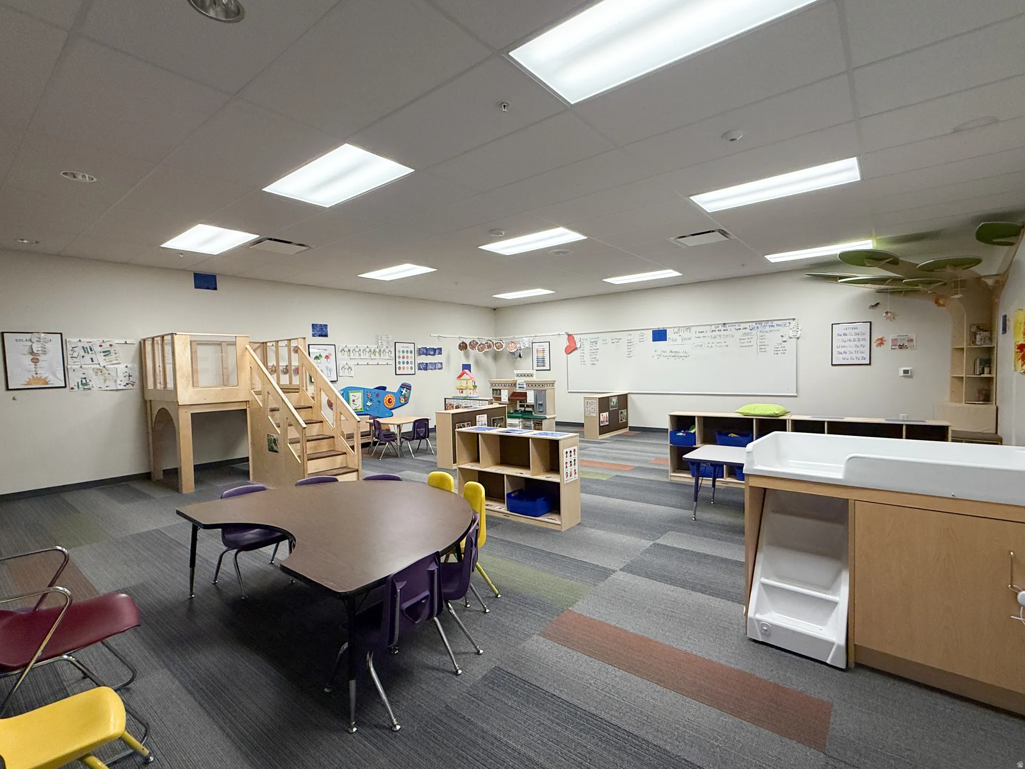 Spacious room featuring patterned carpet flooring and a built-in wooden play structure with stairs