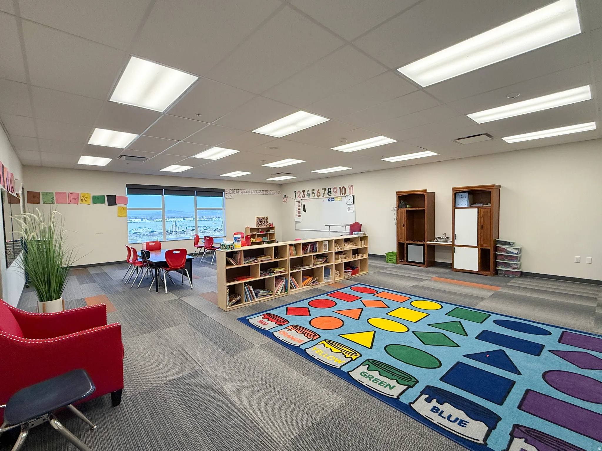 Spacious interior room featuring a large window, drop ceiling with integrated lighting, and modular carpet tile flooring