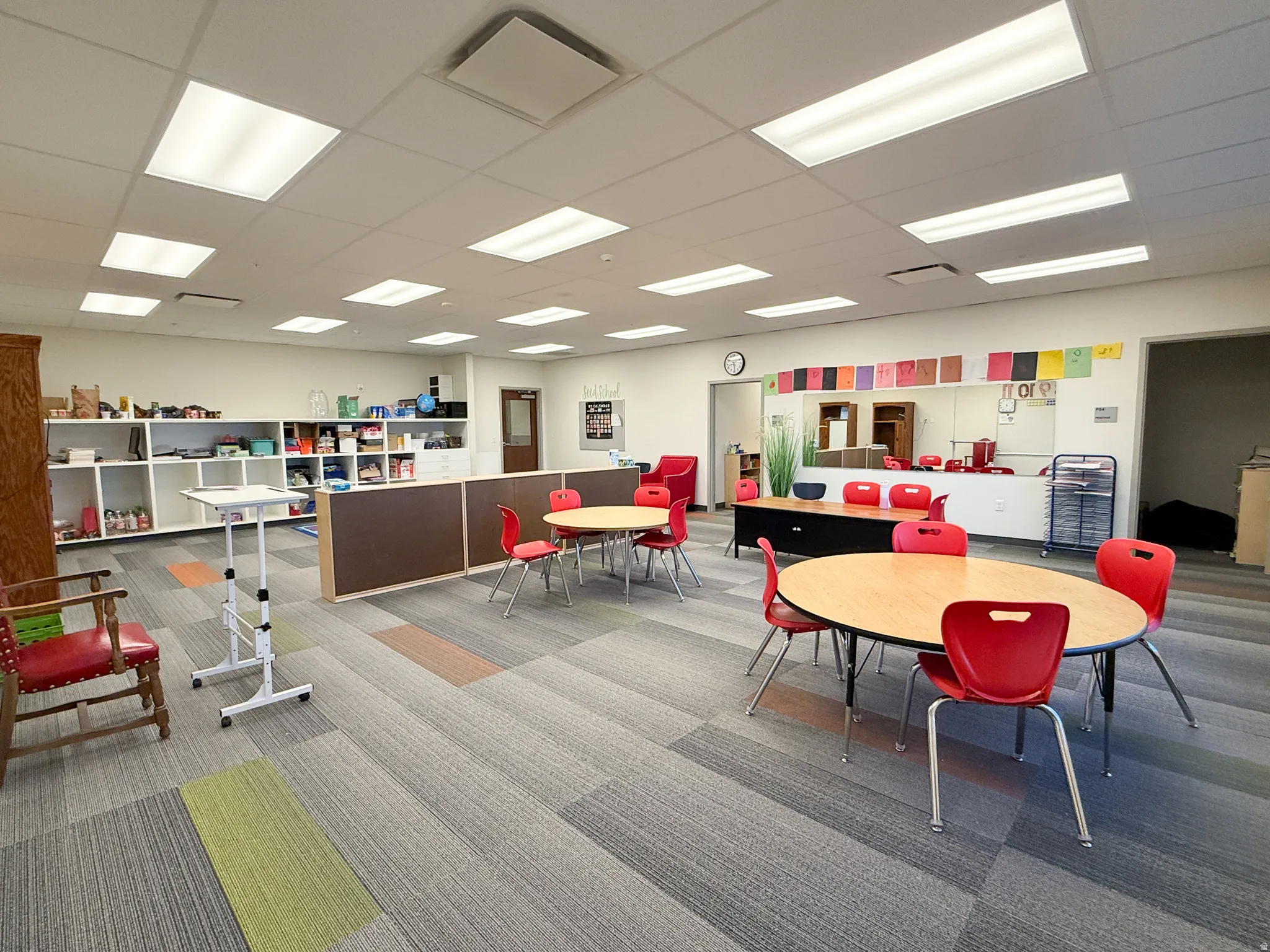 Spacious interior featuring grid ceiling with integrated fluorescent lighting, durable patterned carpet tile flooring, built-in shelving units, and a partial height wall divider