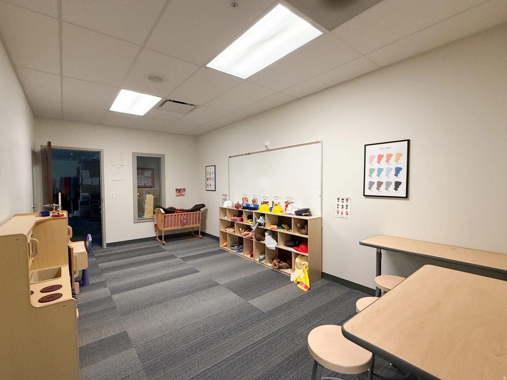 Spacious interior room featuring modular carpet tile flooring, a drop ceiling with recessed lighting, and light-toned walls