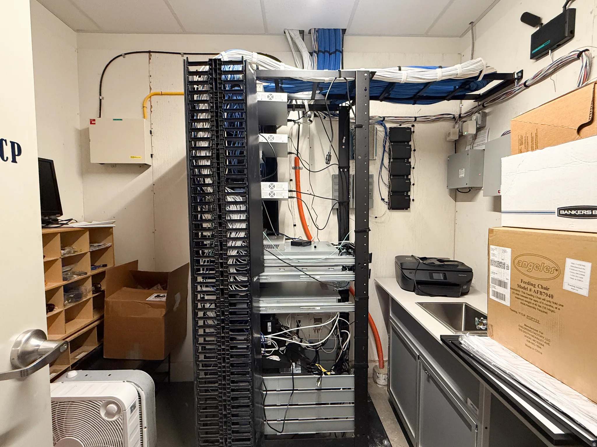 Dedicated utility room featuring extensive network infrastructure with structured cabling, a built-in countertop with an integrated sink, under-cabinet storage, and wood-finish shelving