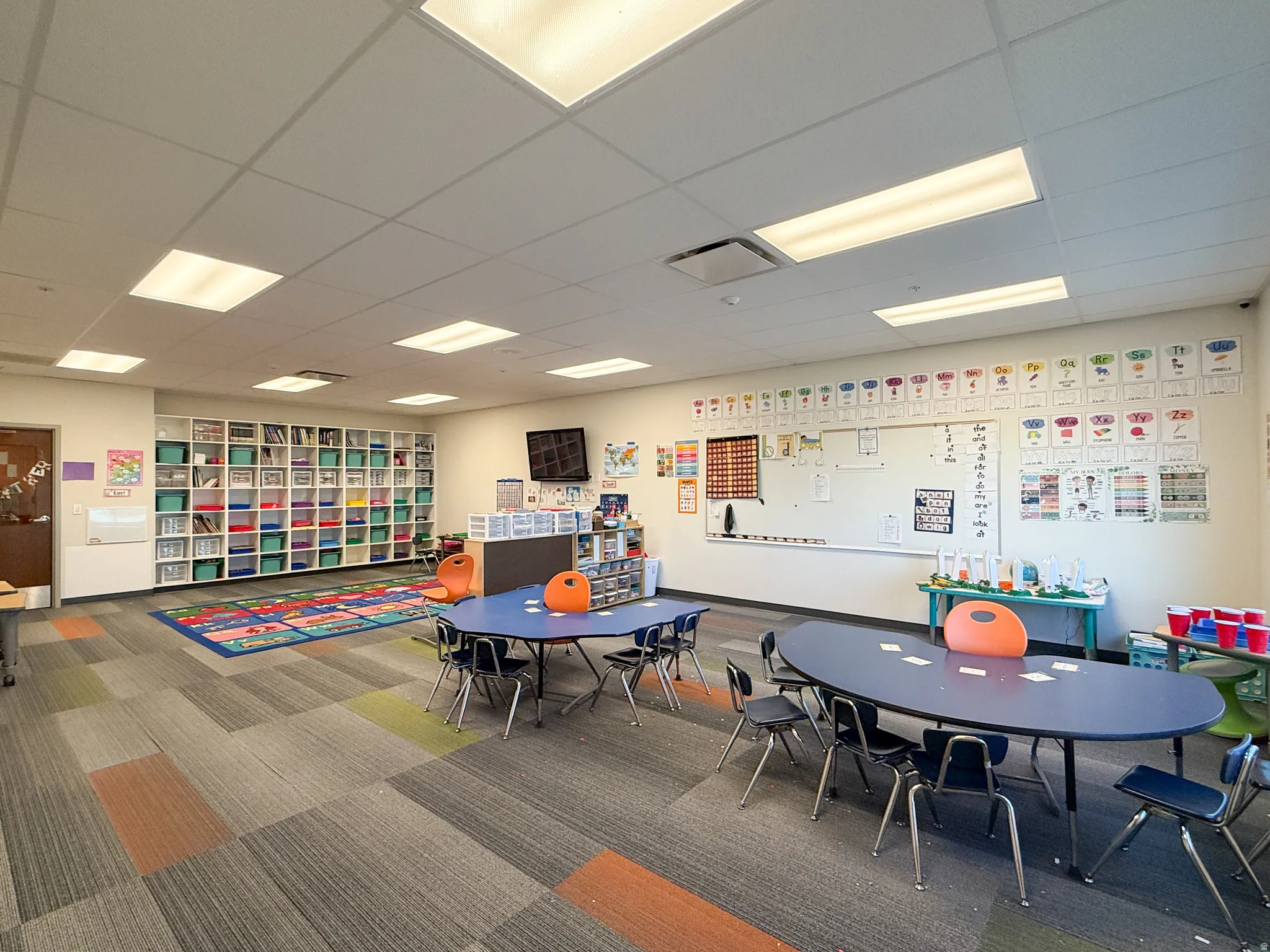 Spacious interior featuring grid ceiling with integrated lighting, built-in shelving, durable patterned carpet, and a large whiteboard