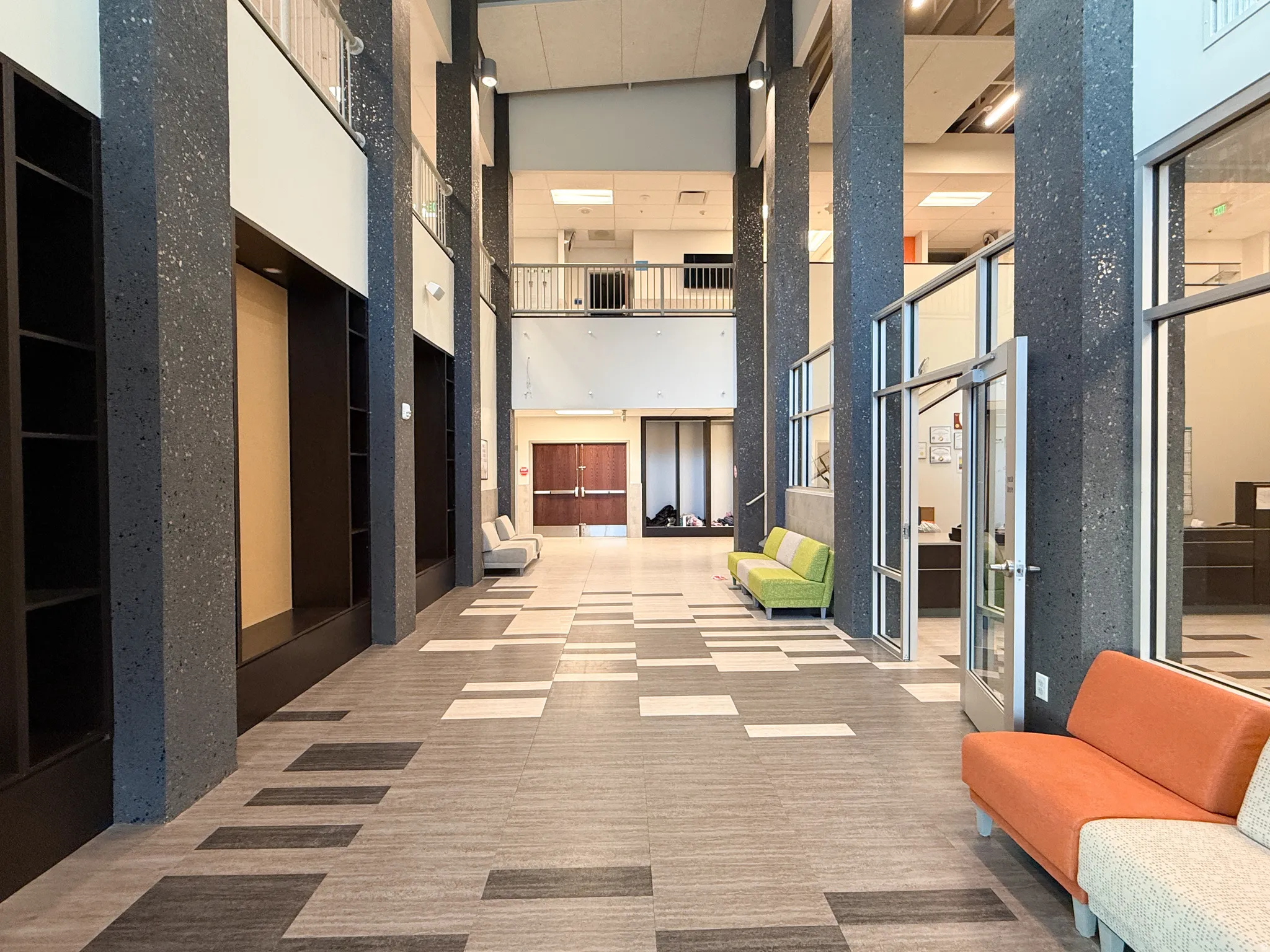 Spacious multi-story lobby featuring patterned tile flooring, exposed aggregate columns, and extensive built-in shelving