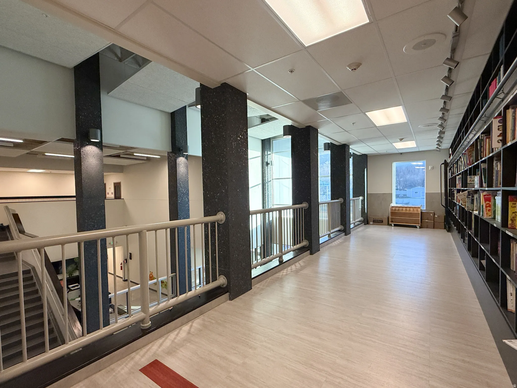 Upper-level hallway featuring light wood-finish flooring, a full-height built-in shelving unit, and a metal railing overlooking a lower level