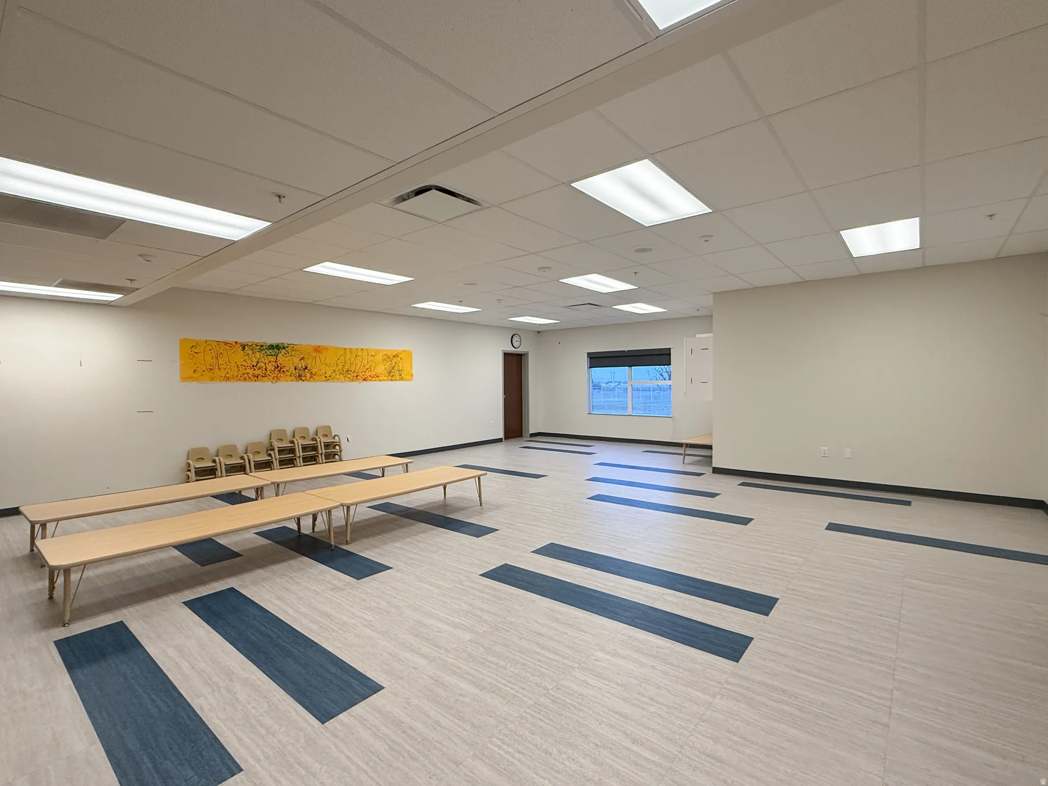 Spacious room featuring light-toned flooring with blue accents, recessed lighting, and a neutral wall palette