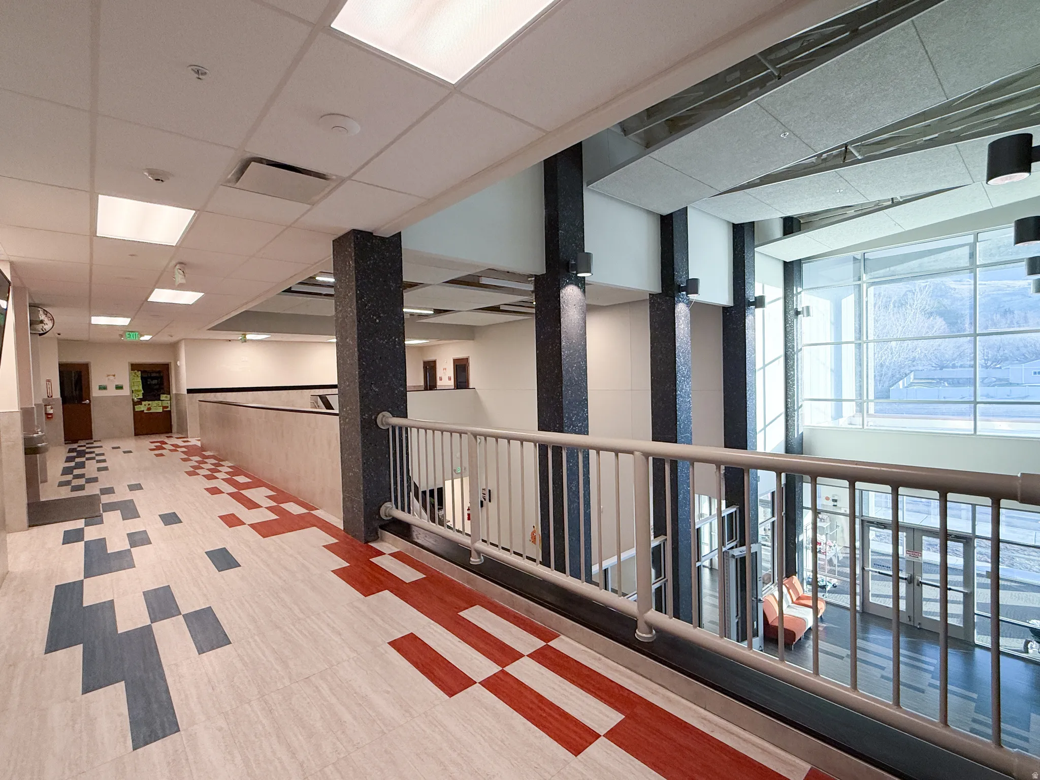 Corridor with patterned flooring, featuring a light-toned railing overlooking a lower level