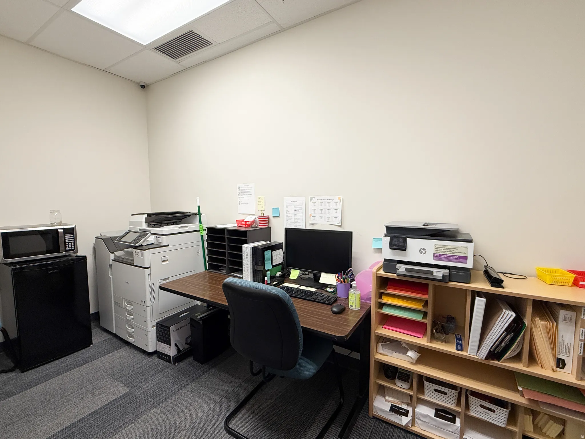 Office space featuring drop ceiling with integrated lighting, textured carpet flooring, and white painted walls