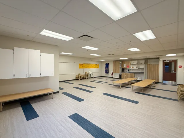 Spacious room featuring light-toned flooring with blue accents, recessed lighting, and a drop ceiling
