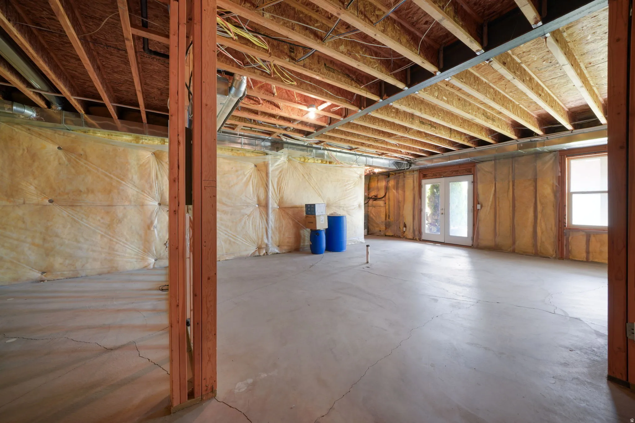 Expansive unfinished basement featuring a concrete floor, exposed wood ceiling joists, and insulated perimeter walls