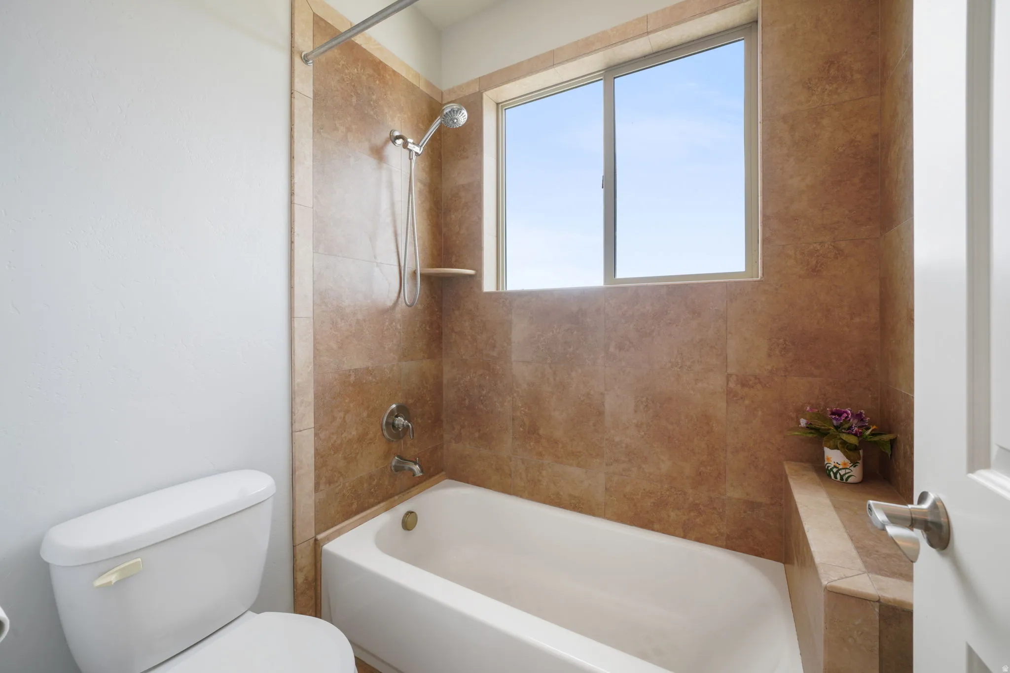 Full bathroom featuring a white bathtub and shower with a tiled surround, a chrome shower head, and a built-in shower niche