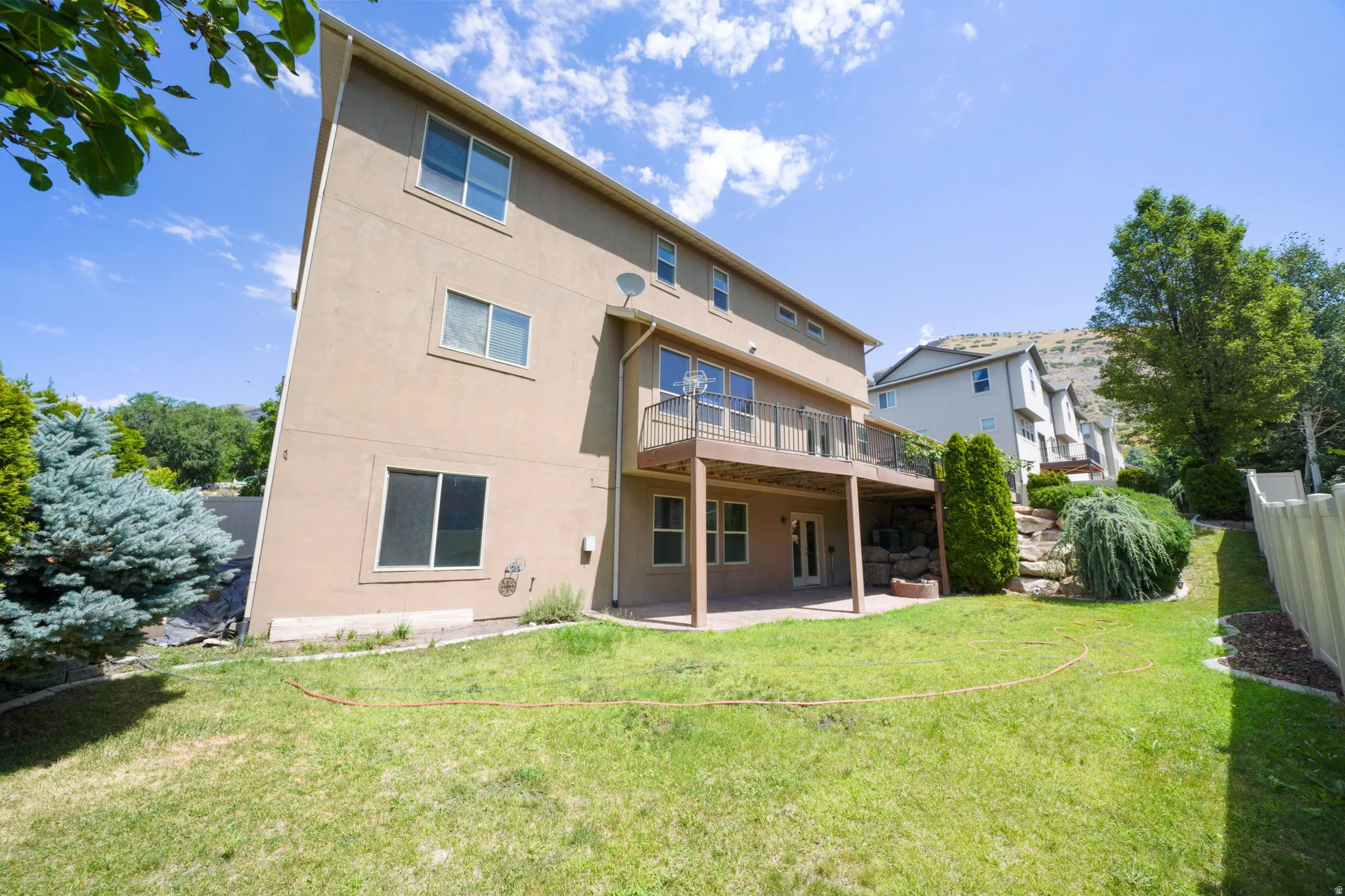Rear exterior featuring a ground-level patio, upper-level deck with black railing, and stucco siding